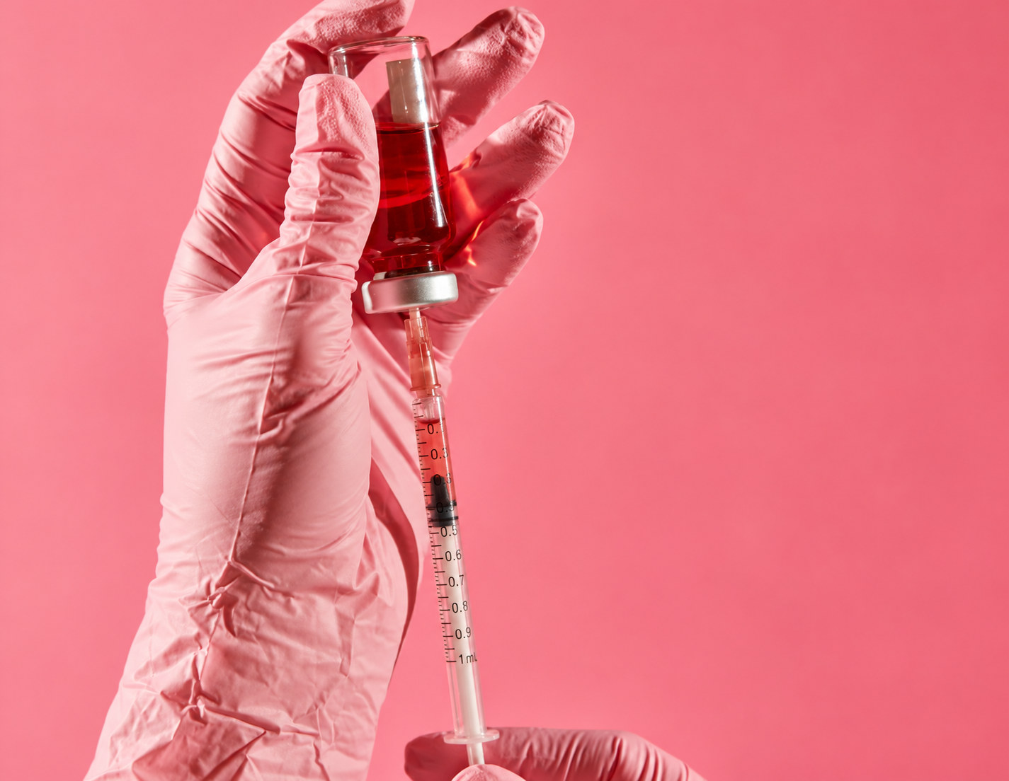 Gloved hands drawing a product from a vial into a syringe against a pink background