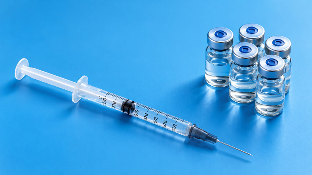 Syringe beside a row of glass vials on a blue background